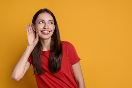 Woman showing hand to ear gesture on orange background, space for textの写真素材