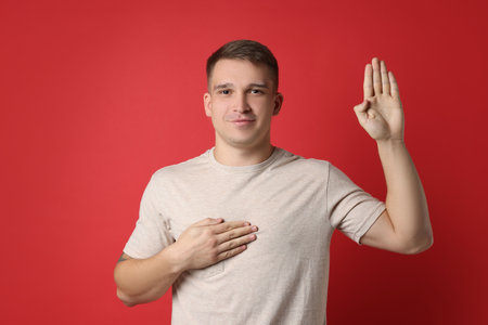 Man making promise with raised hand on red background. Oath gestureの写真素材