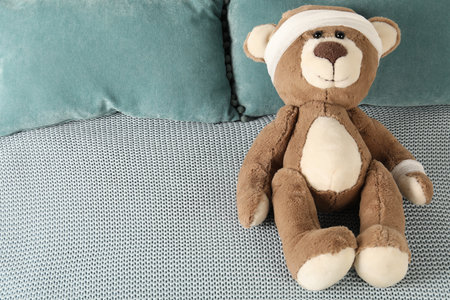 Cute teddy bear with bandages on bed, top view. Space for text