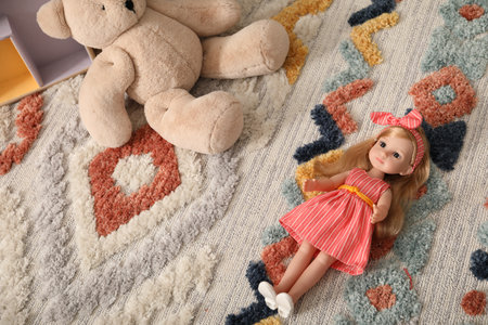 Beautiful doll in dress and teddy bear on soft carpetの写真素材