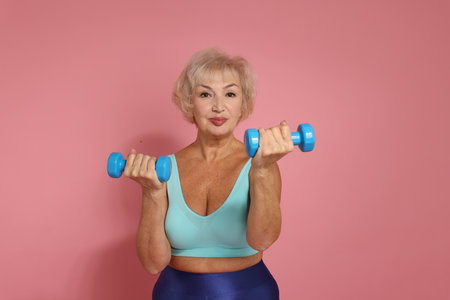 Senior woman exercising with dumbbells on pink backgroundの写真素材