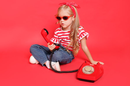 Cute little girl with telephone on red backgroundの写真素材