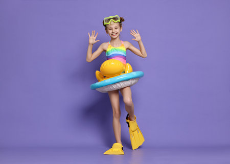 Happy girl in beachwear with diving mask, flippers and inflatable ring on purple backgroundの写真素材