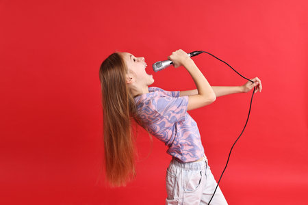 Little girl with microphone singing on red backgroundの写真素材