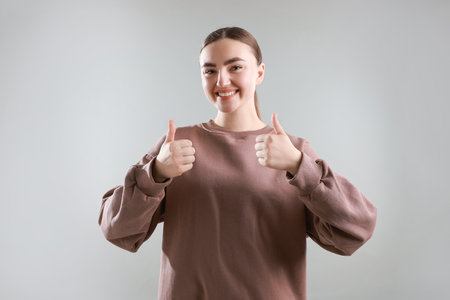Happy woman showing thumbs up on grey background. Like gestureの写真素材