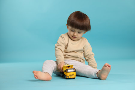Cute little boy playing with toy truck on light blue backgroundの写真素材