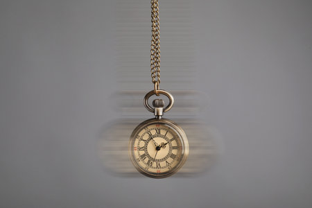 Hypnosis session. Vintage pocket watch swinging on grey background, motion blur effect