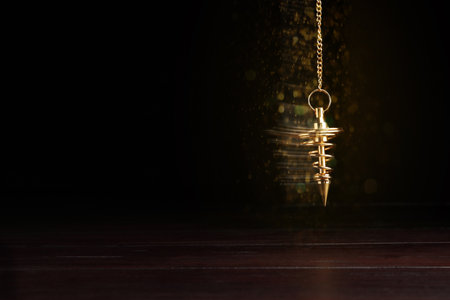 Hypnosis session. Golden pendulum swinging on black background, motion blur effect. Magic lights