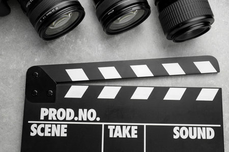 Movie clapper and camera lens on gray textured table, flat layの写真素材