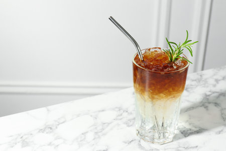 Refreshing espresso tonic drink with rosemary on white marble table, space for text