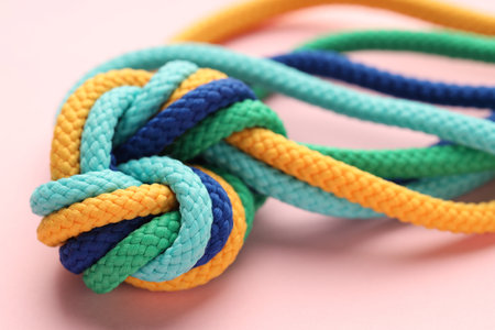 Colorful ropes tied in knot on light pink background, closeup. Unity concept