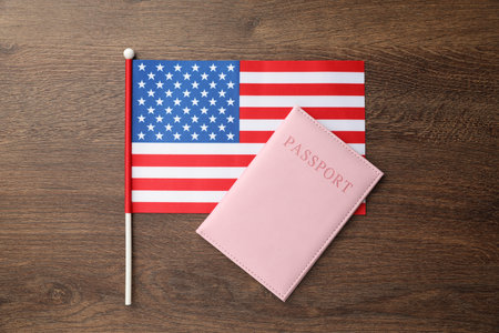 Passport in pink cover and flag of United States on wooden table, top view