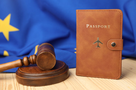 Passport in brown cover, judge's gavel and flag of European Union on wooden table, closeup