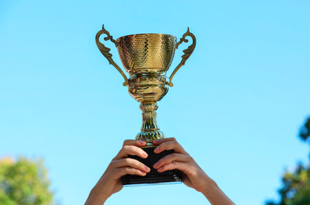 Woman holding golden trophy against blue sky outdoors, closeupの写真素材