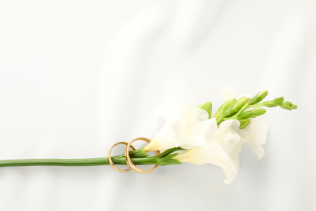 Golden wedding rings and flowers on white fabric, top viewの写真素材