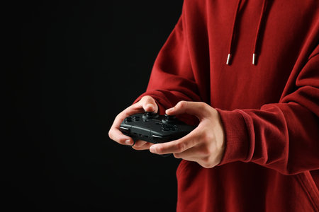 Teenage boy playing video game with controller on black background, closeup. Space for text