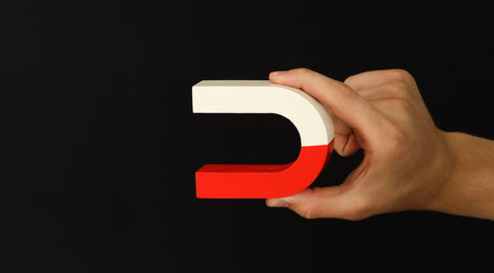 Man with horseshoe magnet on dark background, closeup. Space for text