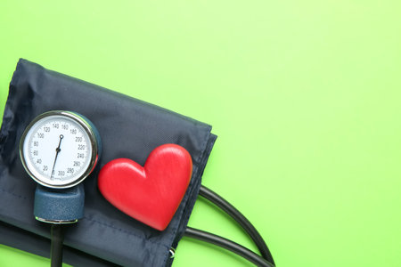 Blood pressure measuring device and heart figure on green background, top view. Space for text