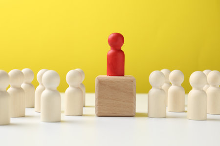 Human figures around wooden block with red figure on top against yellow background. Competition conceptの写真素材