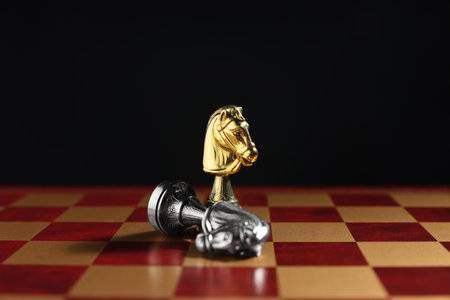 Golden knight and fallen silver one on chessboard against black background, closeup. Competition...