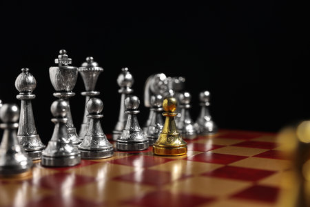 Golden pawn in front of silver chess pieces on chessboard against black background, closeup. Competition conceptの写真素材