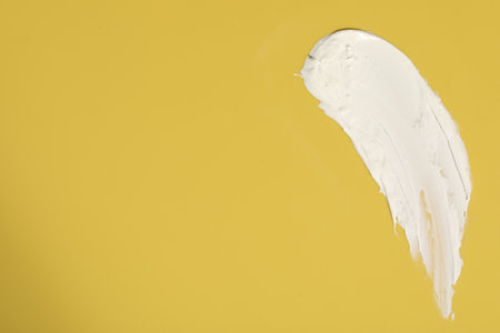 Cream on yellow background, top view and space for text. Sample of cosmetic product