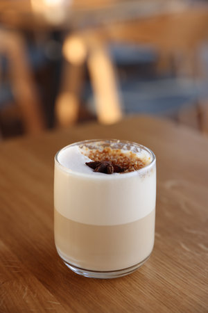 Glass of aromatic coffee on wooden table in cafe, closeup. Space for text