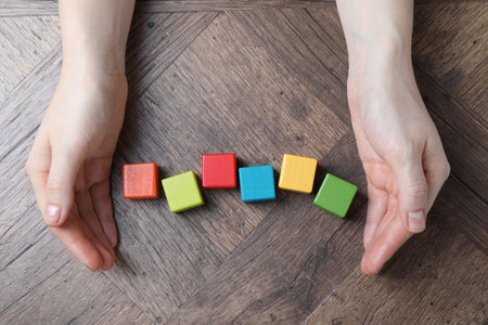 Woman with colorful cubes at wooden table, top view