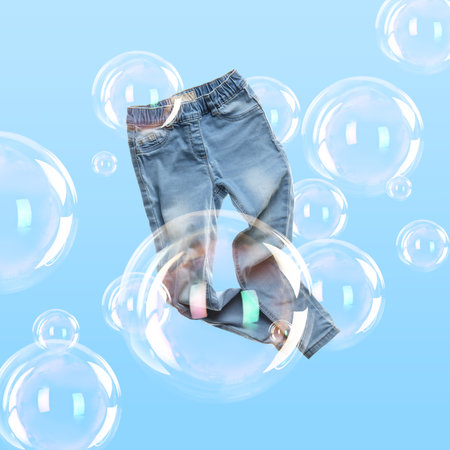 Jeans flying among soap bubbles on light blue background. Laundry dayの写真素材