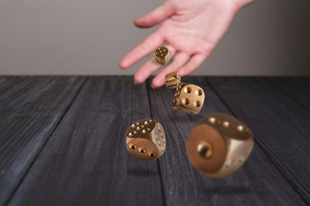 Woman throwing gold dice on black wooden table, closeup. Space for text