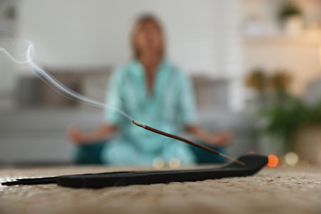 Incense stick smoldering in holder on mat indoors, selective focusの写真素材