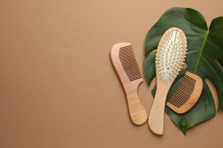 Wooden hair brush, combs and monstera leaf on dark beige background, flat lay. Space for textの写真素材