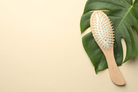 Wooden hair brush and monstera leaf on beige background, top view. Space for textの写真素材
