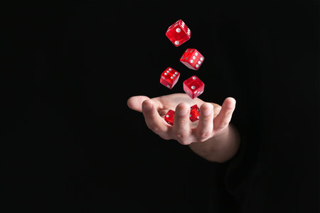 Man throwing red dice in darkness, closeup. Space for textの写真素材