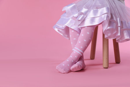 Child in tights sitting on stool against pink background, closeup. Space for textの写真素材