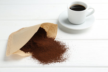 Paper filter, ground coffee and cup of drink on white wooden tableの写真素材