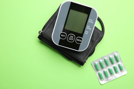 Blood pressure measuring device and pills on green background, top view
