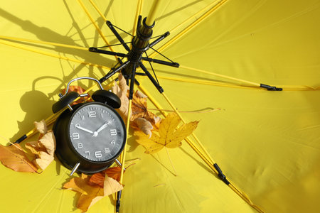 Alarm clock and dry leaves on yellow umbrella, closeup. Space for textの写真素材