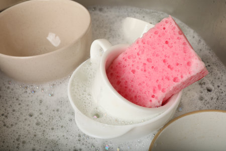 Pink sponge, dishes and foam in sink, closeupの写真素材