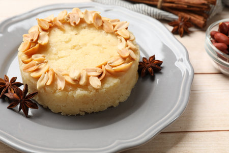 Delicious semolina halva with almond flakes and spices on white wooden table, closeup