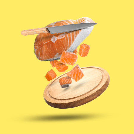 Red fish pieces, knife and cutting board falling on yellow backgroundの写真素材