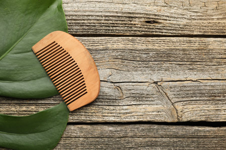 Comb and monstera leaf on wooden table, top view. Space for text