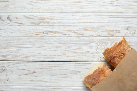 Paper bag with halves of fresh baguette on wooden table, top view. Space for textの写真素材