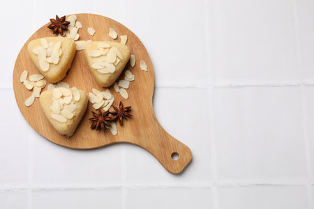 Pieces of sweet semolina halva with almond flakes on white tiled table, top view. Space for text