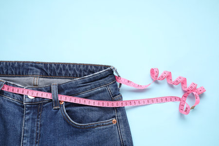 Jeans and measuring tape on light blue background, top view. Space for textの写真素材