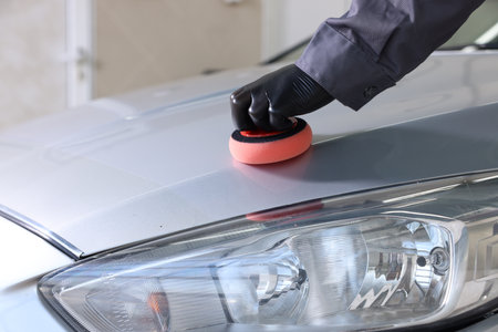 Man polishing car hood with sponge indoors, closeupの写真素材