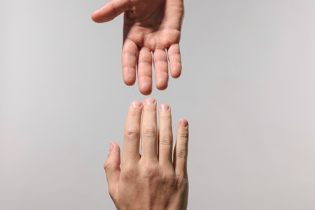 Two hands reaching toward each other on light grey background, closeupの写真素材