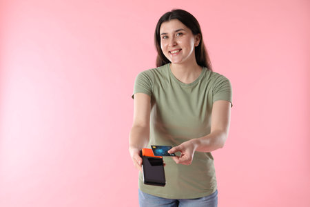 Person with payment terminal and debit card on pink background, space for text