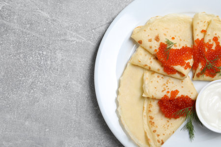 Tasty crepes with red caviar, dill and sauce on grey textured table, top viewの写真素材