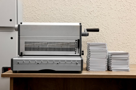 Modern binding machine and stacks of notebooks on wooden table indoors